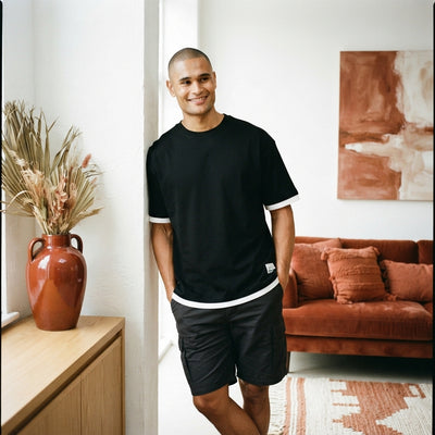 A man wearing a black premium oversized t-shirt in a modern living room with terracotta and burnt sienna decor.
